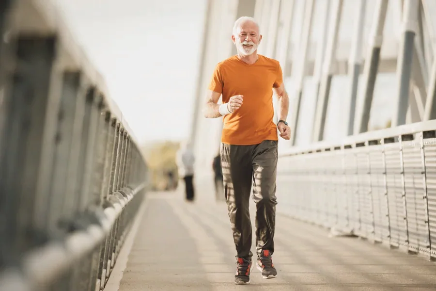 An older man in an orange shirt walking briskly across a footbridge